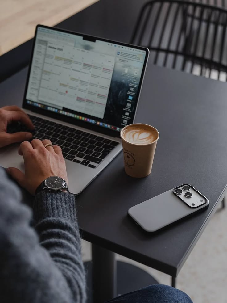 Persona trabajando en un laptop con una base de contactos comercial abierta junto a un café